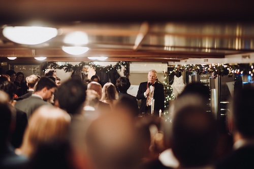 Event speaker addressing guests with a microphone during a corporate Christmas party on a private Thames boat