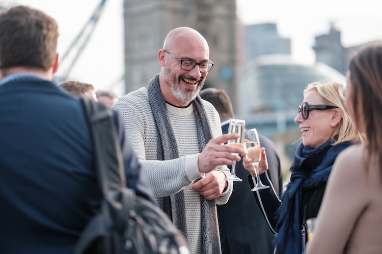 Corporate guests enjoying drinks and clinking champagne glasses on the vessel outer deck during a networking reception on the Thames.