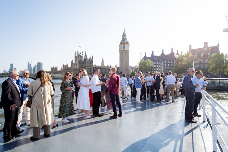 Colleagues engaging in relaxed conversation on the outdoor deck of a private West End on the Thames vessel to build team culture.